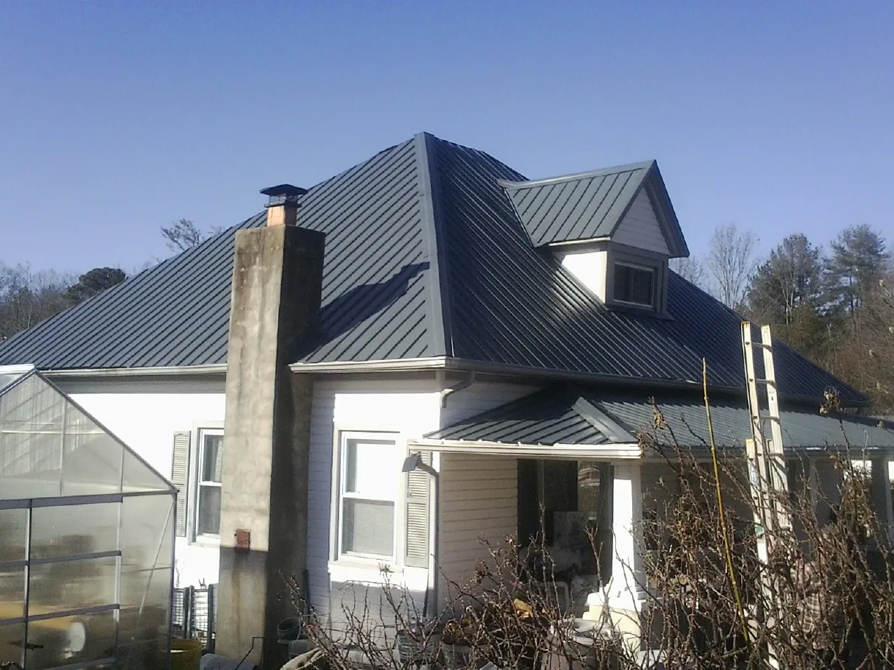 Dark blue standing seam metal roof on a white farmhouse with dormer — Slate & Tile Roof Repair by Roofing Brothers in Mcdaniel