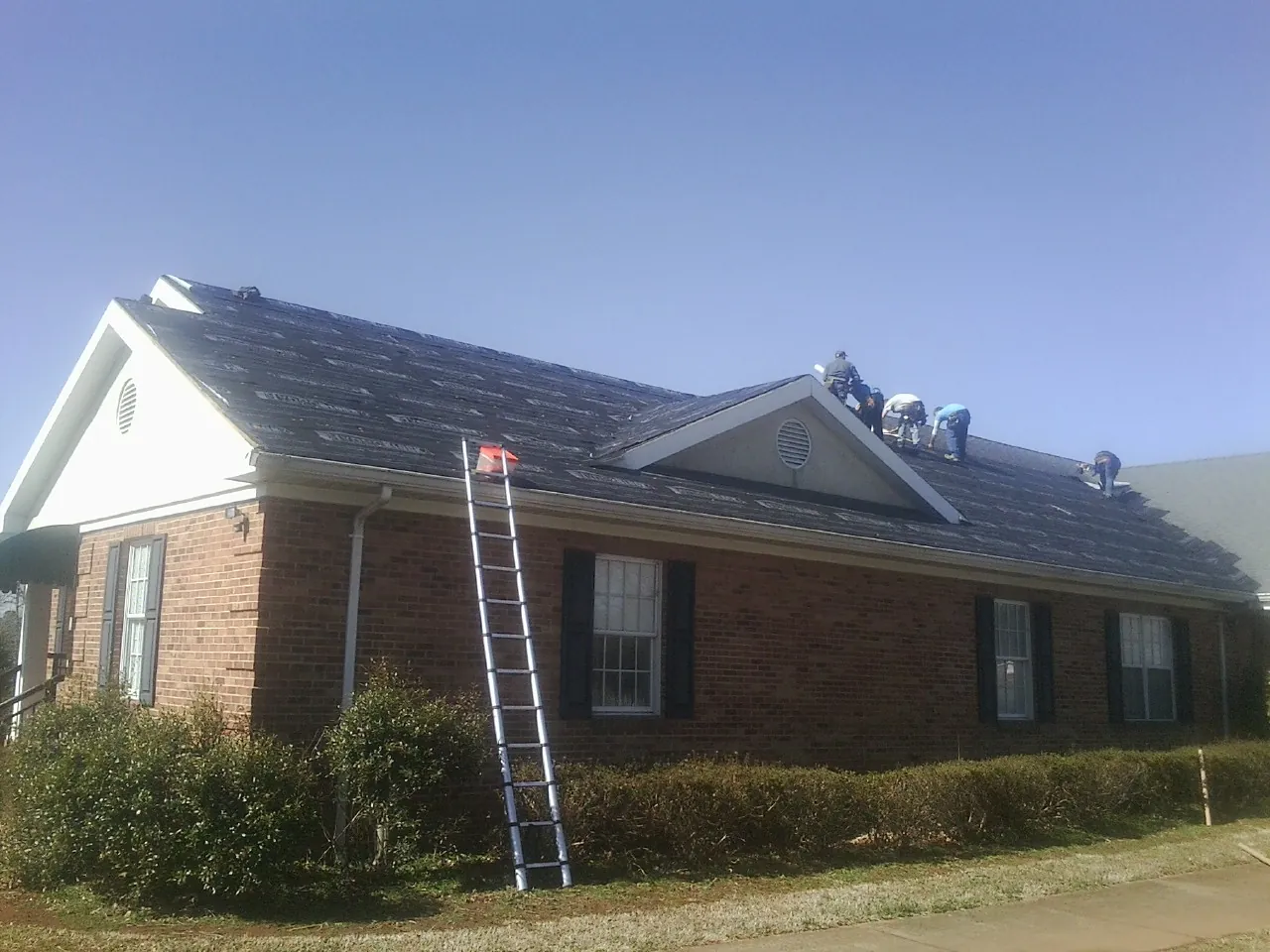Crew tearing shingles off a brick ranch roof with a ladder set — Metal Roof Repair work by our crew in Mcdaniel