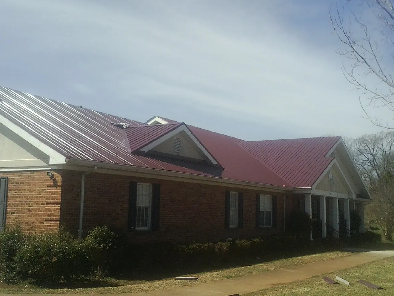 Red metal roof with gabled entries on a long brick building, from a Hail Damage Roof Repair job in Mcdaniel