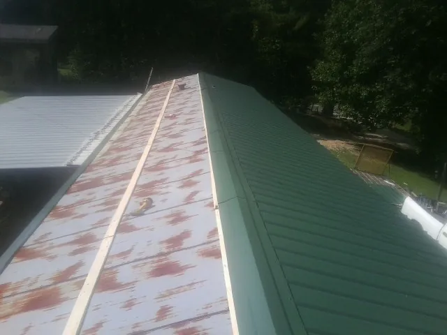 Old rusted panels beside newly installed green metal roofing — Wind Damage Roof Repair by Roofing Brothers in Mcdaniel