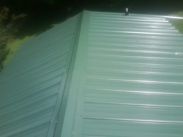 New green metal panels meeting at the ridge of a roof — Flat Roof Repair work by our crew in Mcdaniel